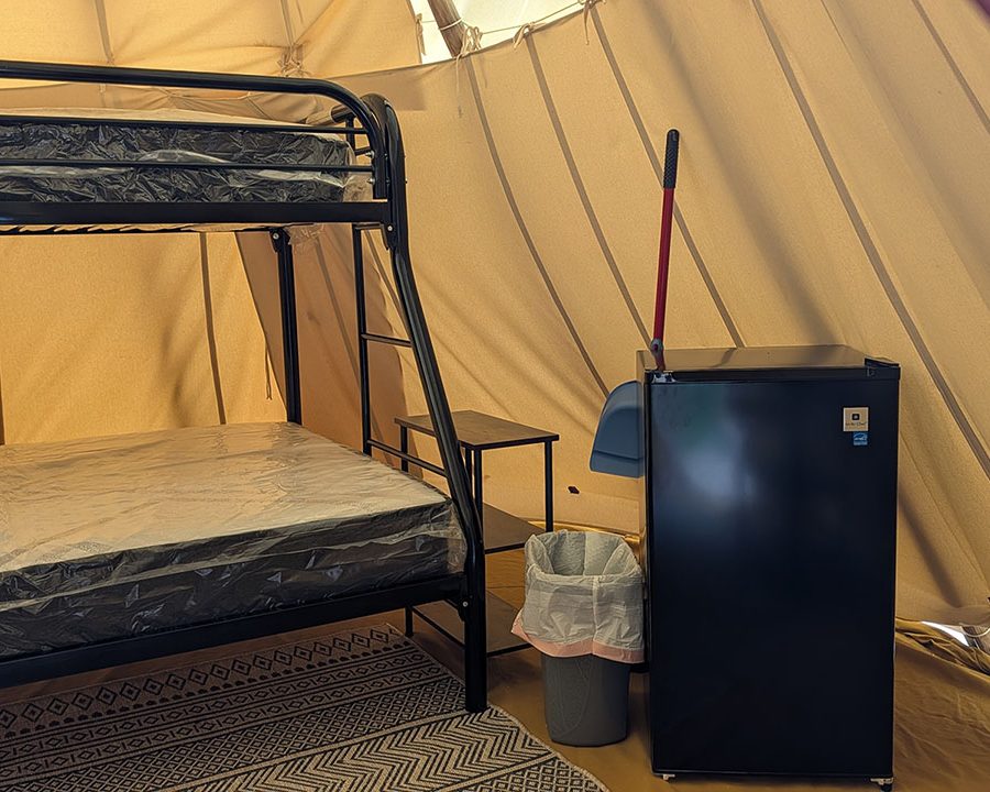 Tipi interior with bunk bed and refrigerator at Crystal Rock Campground